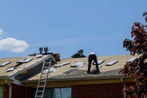 A worker carefully installs solar panels on a shingle roof under bright sunlight.