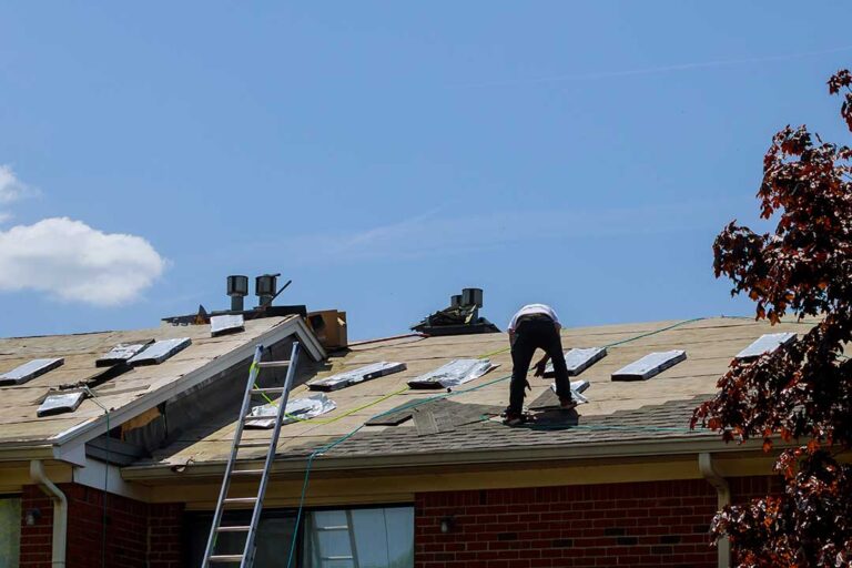 A worker carefully installs solar panels on a shingle roof under bright sunlight.